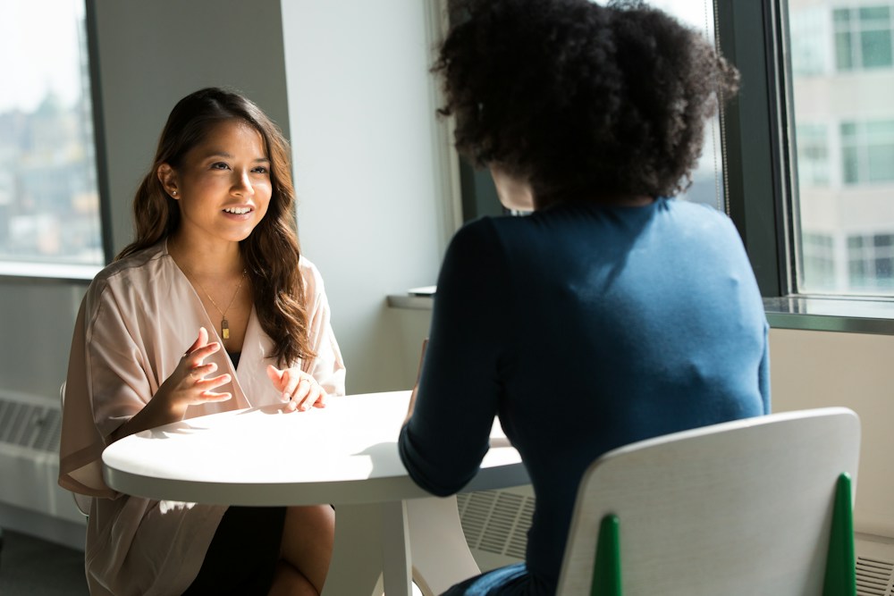 Duas mulheres conversam em um ambiente de atendimento; imagem ilustrativa